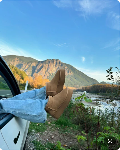 A relaxing road trip scene showing someone resting their feet, clad in tan boots, out of a car window while overlooking a beautiful mountain landscape