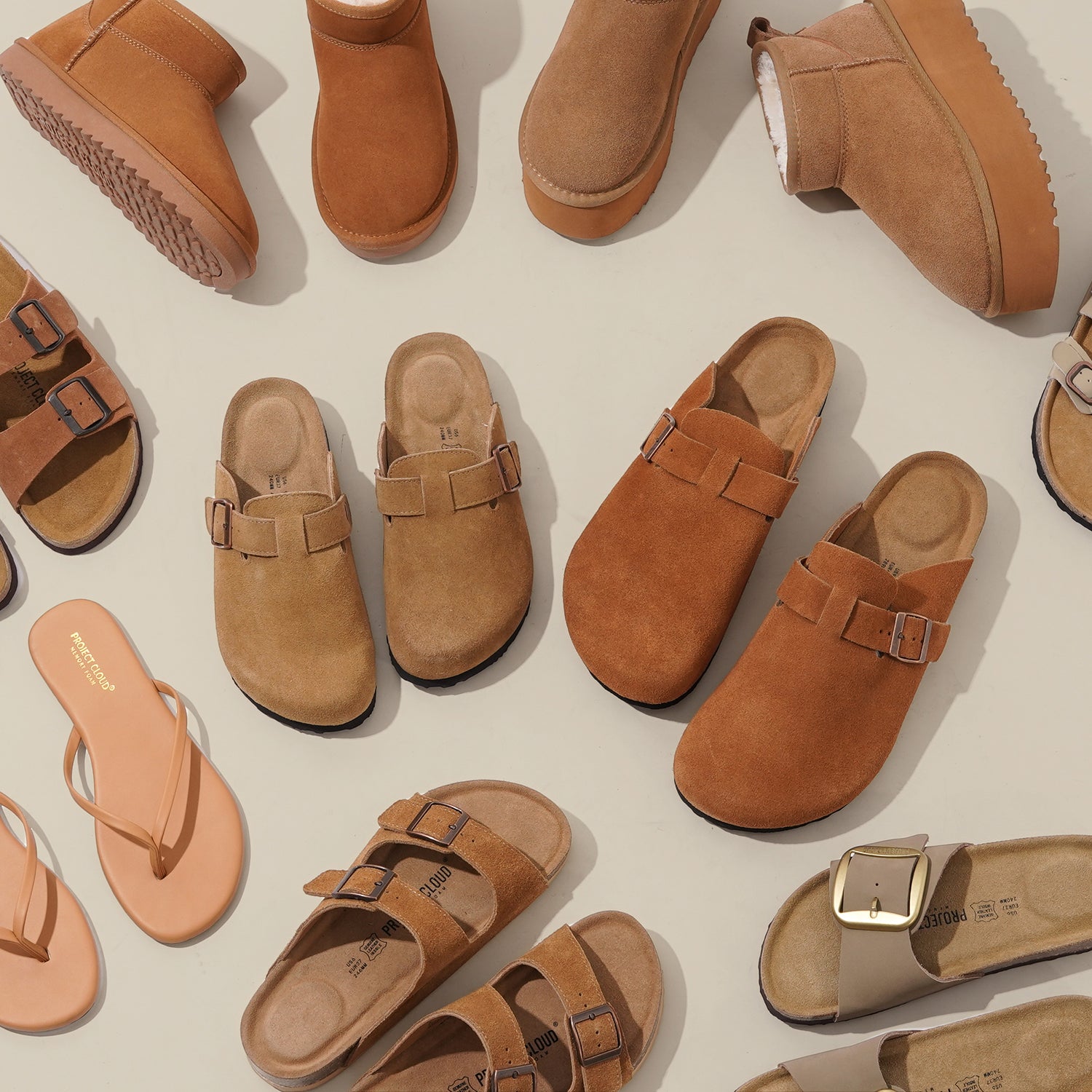 Taupe suede slip-on clogs with a stylish bronze buckle, featuring a cork footbed and black sole, placed on a textured beige and white area rug for a casual and cozy look.
