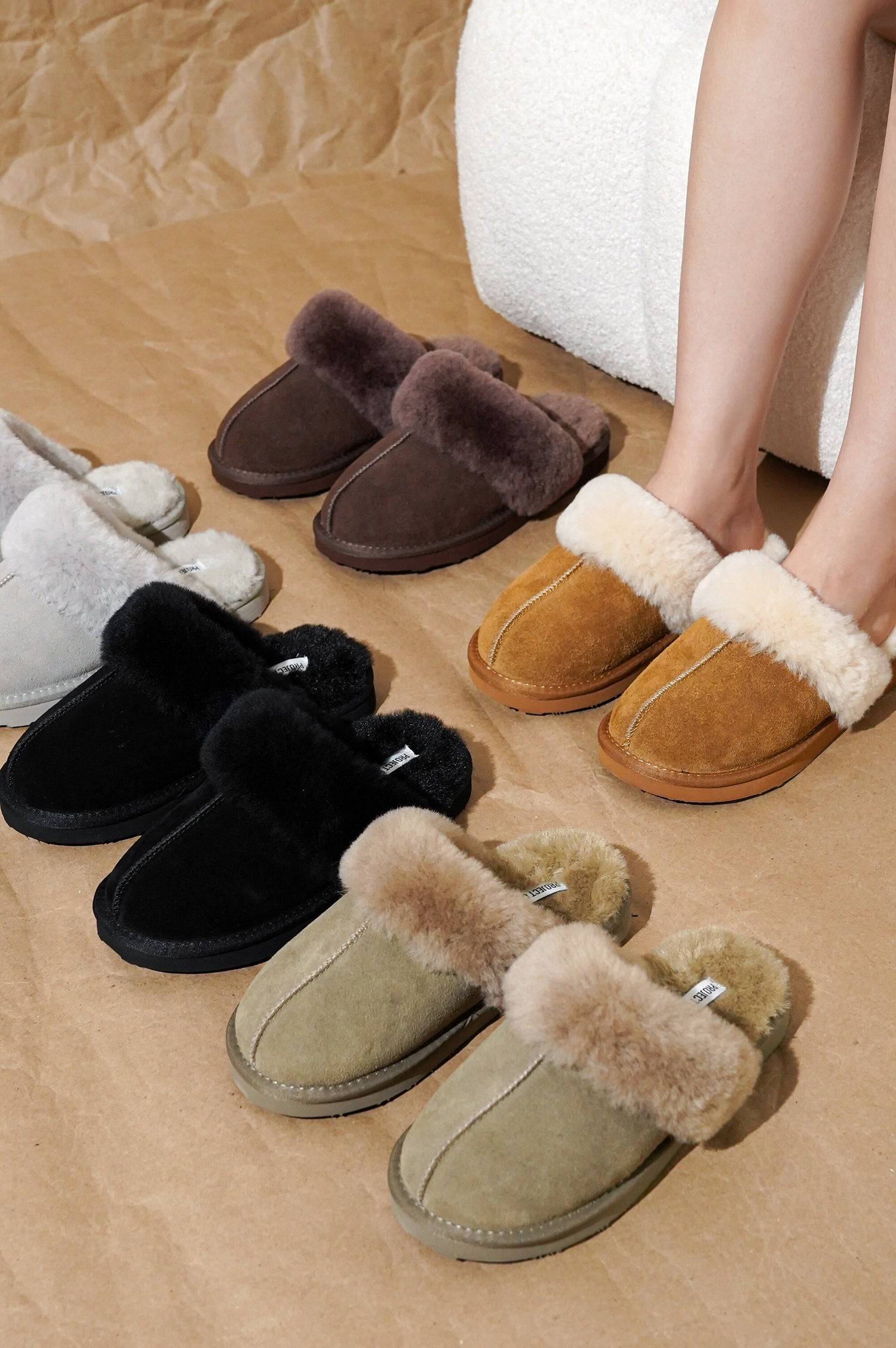 Collection of shearling slippers in various colors including black, white, brown, beige, and gray arranged on wooden floor