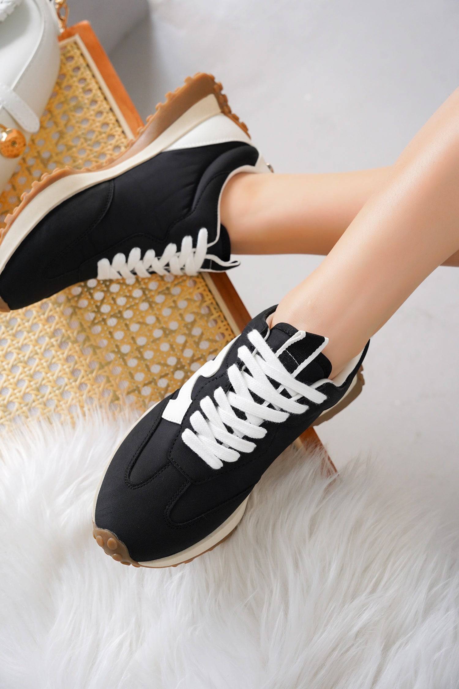 Black Lecco women's sneakers with white laces, memory foam, and non-slip sole on a white fur rug.