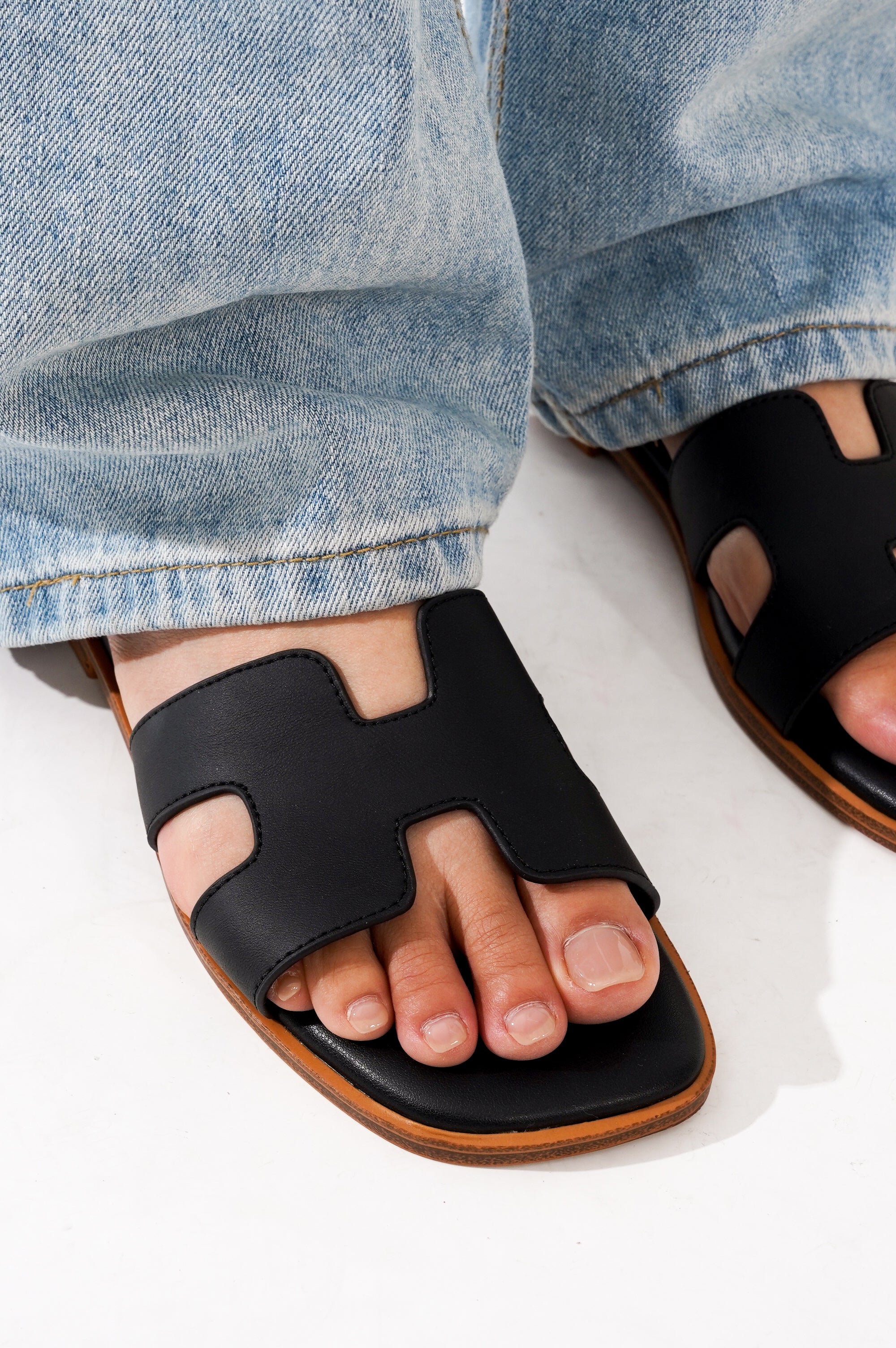 Black leather Jannel sandals on foot, worn with jeans, perfect for summer style and comfort.